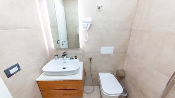 A bathroom with a sink, mirror, toilet, and a hairdryer mounted on the wall.