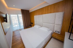 Una habitación de hotel moderna con una cama grande, paneles de madera en las paredes, un televisor de pantalla plana montado en la pared y una mesita de noche de madera.