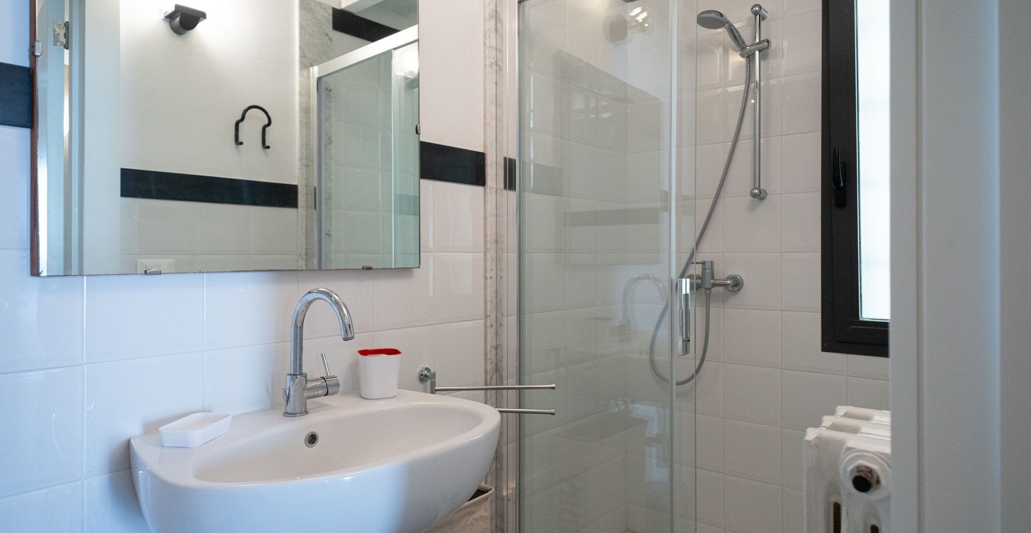 A modern bathroom with a white sink, a mirror, and a glass-enclosed shower area.