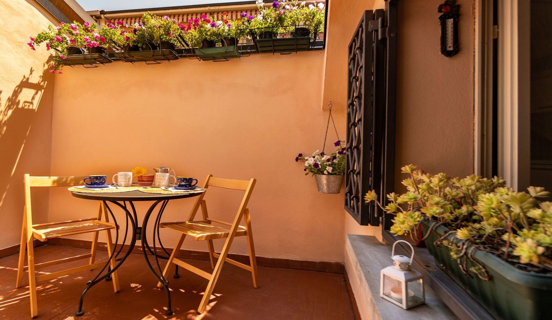 A small outdoor seating area with a table and chairs, a hanging flower basket, and a potted plant.