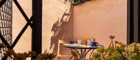 Un patio soleado con una mesa dispuesta para dos personas, que incluye una silla y una mesita.