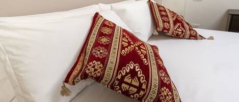 A bed with white linens and two decorative pillows with intricate patterns.