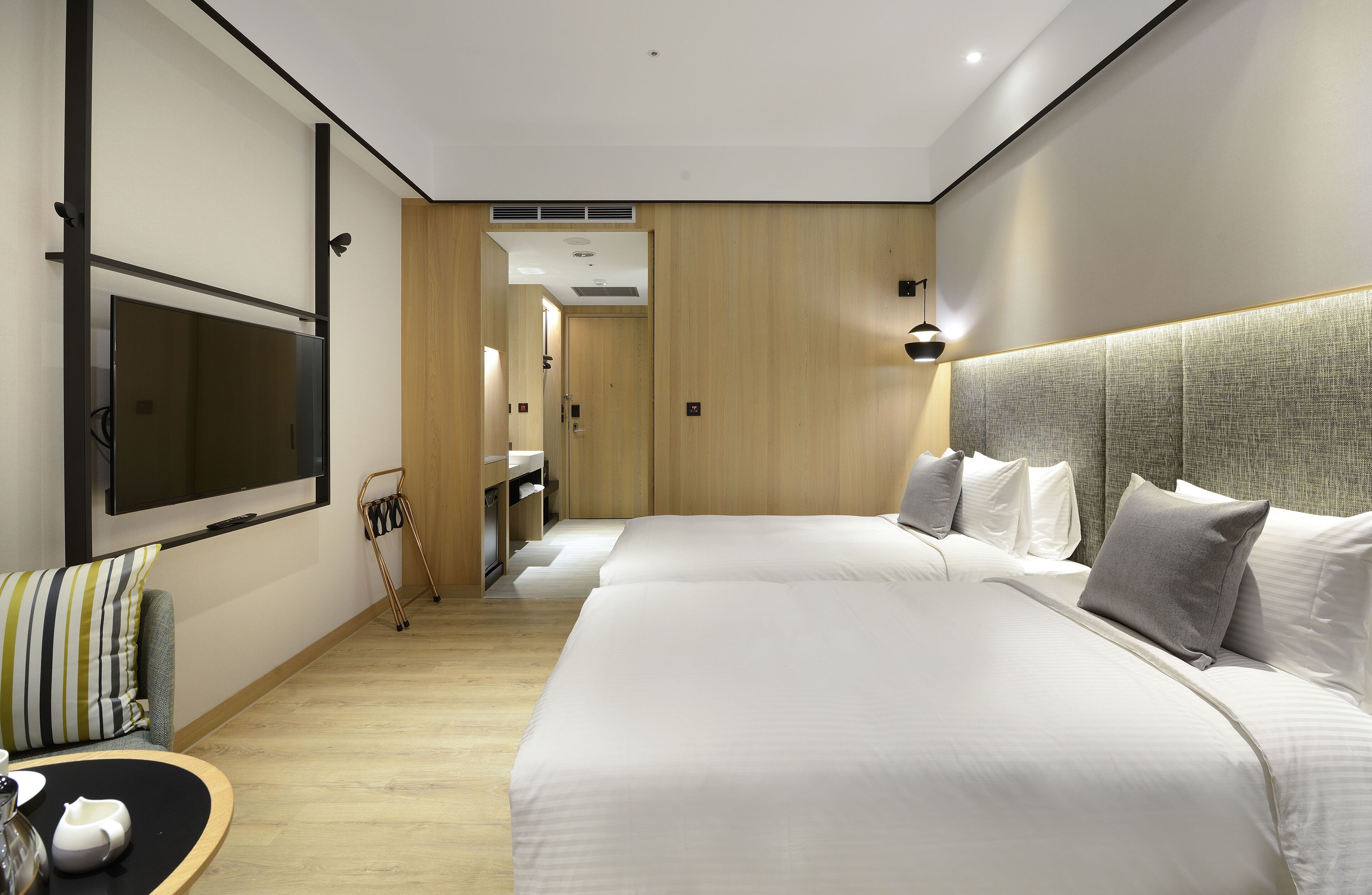 A modern hotel room with a large bed, a TV mounted on the wall, a seating area with a table, and a wooden floor.