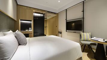 A hotel room with a large bed, a desk with a chair, a TV, and a wardrobe.