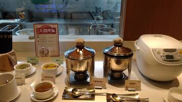 A kitchen area with stainless steel containers labeled for different dishes, a rice cooker, and utensils on a counter.