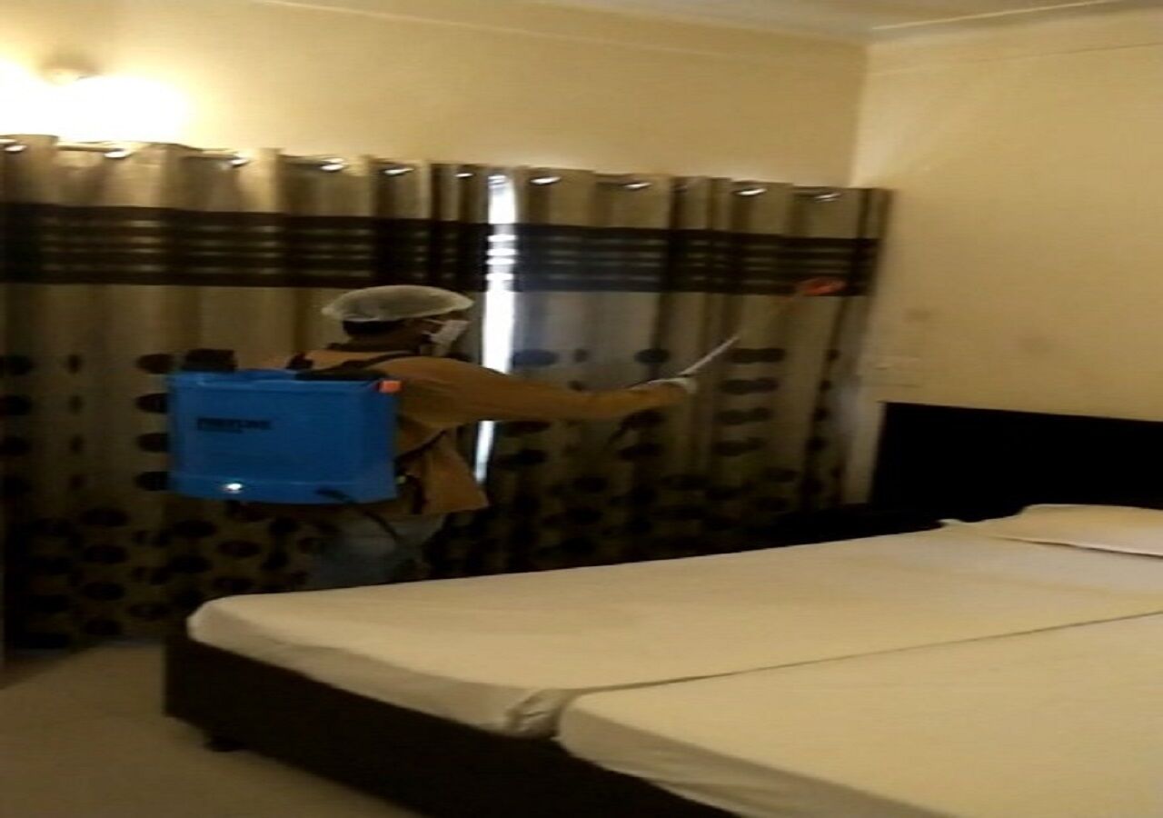A hotel room with a bed, curtains, and a person cleaning.