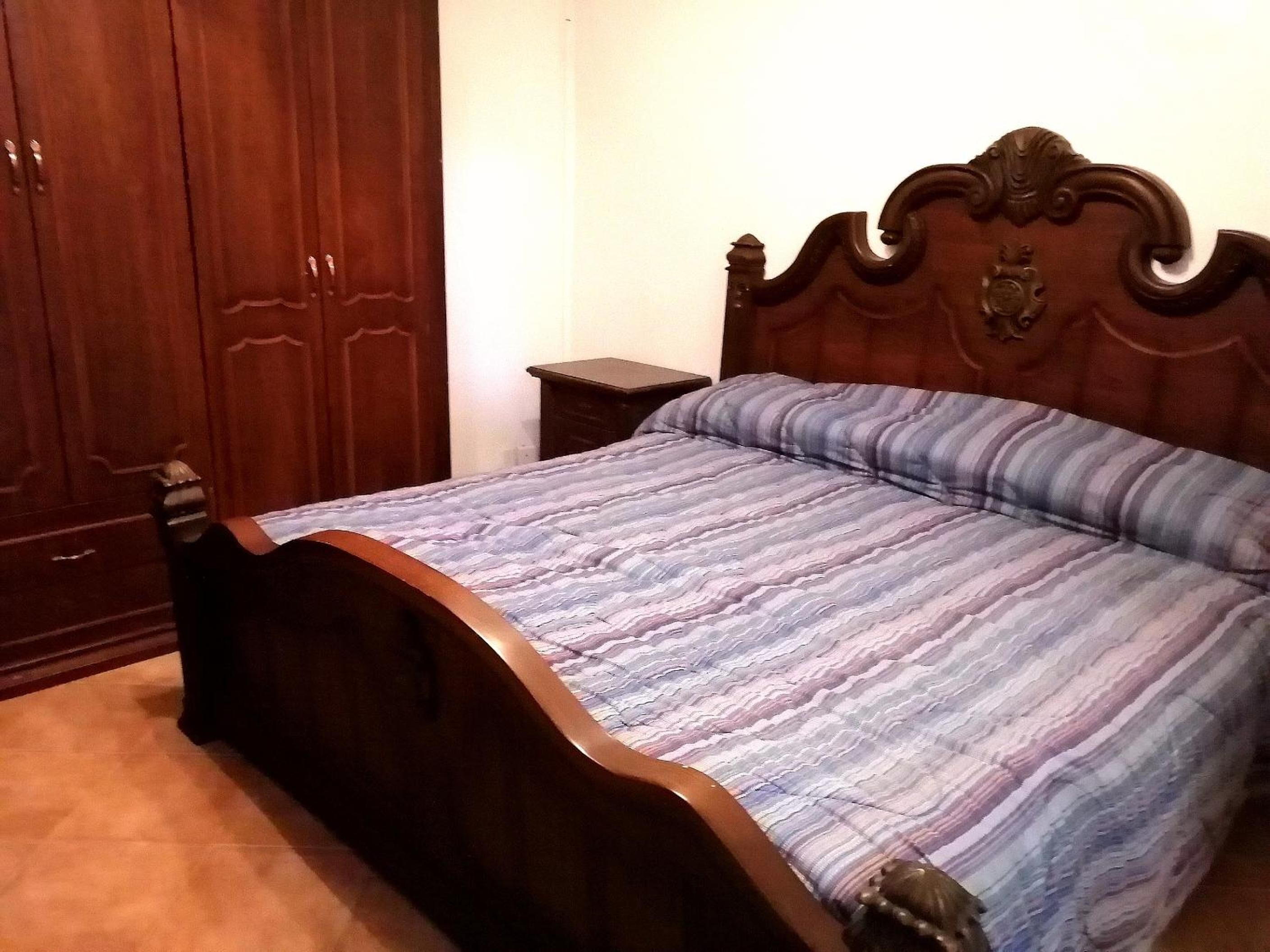 Een slaapkamer met een houten bed, een nachtkastje en een garderobe.