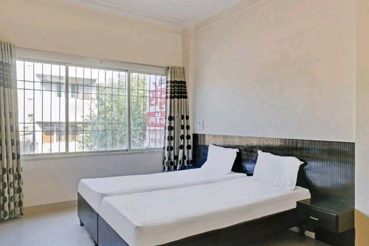 A bedroom with a large window, a bed, a nightstand, and a wall-mounted shelf.