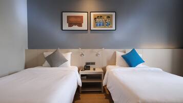 Habitación de hotel con dos camas, una mesita de noche con teléfono y lámpara, y dos cuadros en la pared.