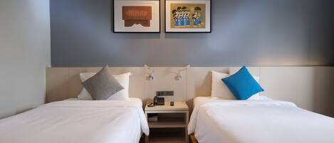 A hotel room with two beds, a nightstand with a phone and lamp, and two framed pictures on the wall.