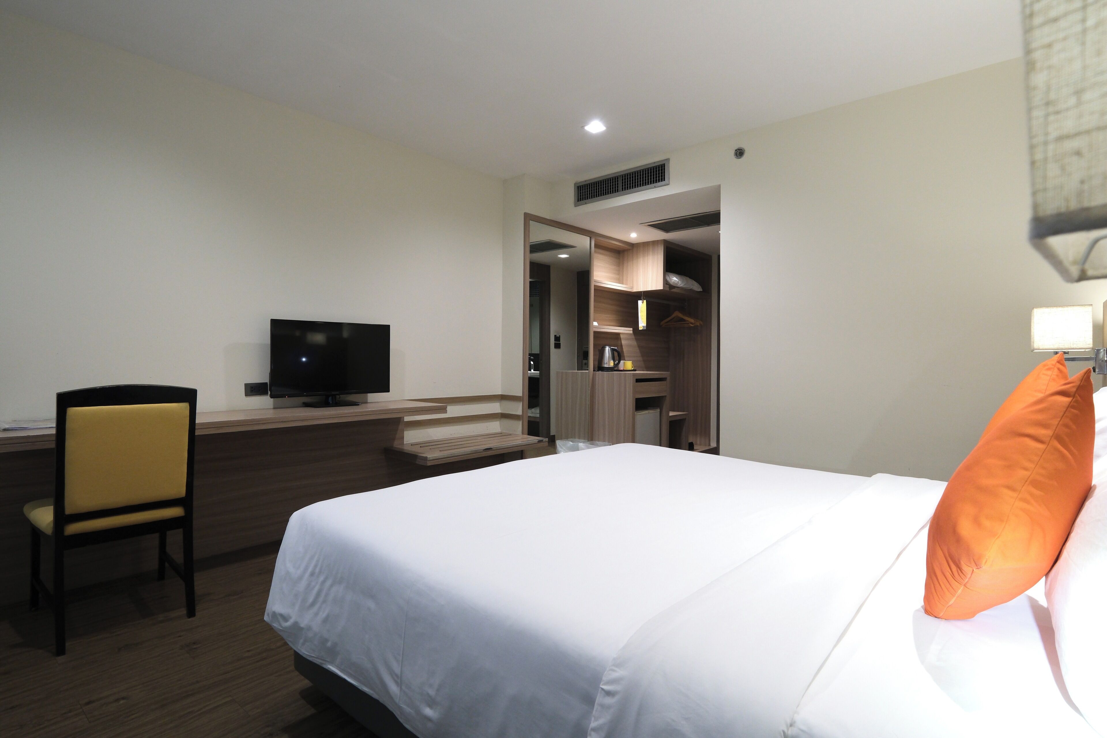 Una habitación de hotel con cama, escritorio, silla, televisor y armario.