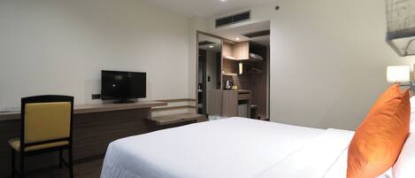 Una habitación de hotel con cama, escritorio, silla, televisor y armario.
