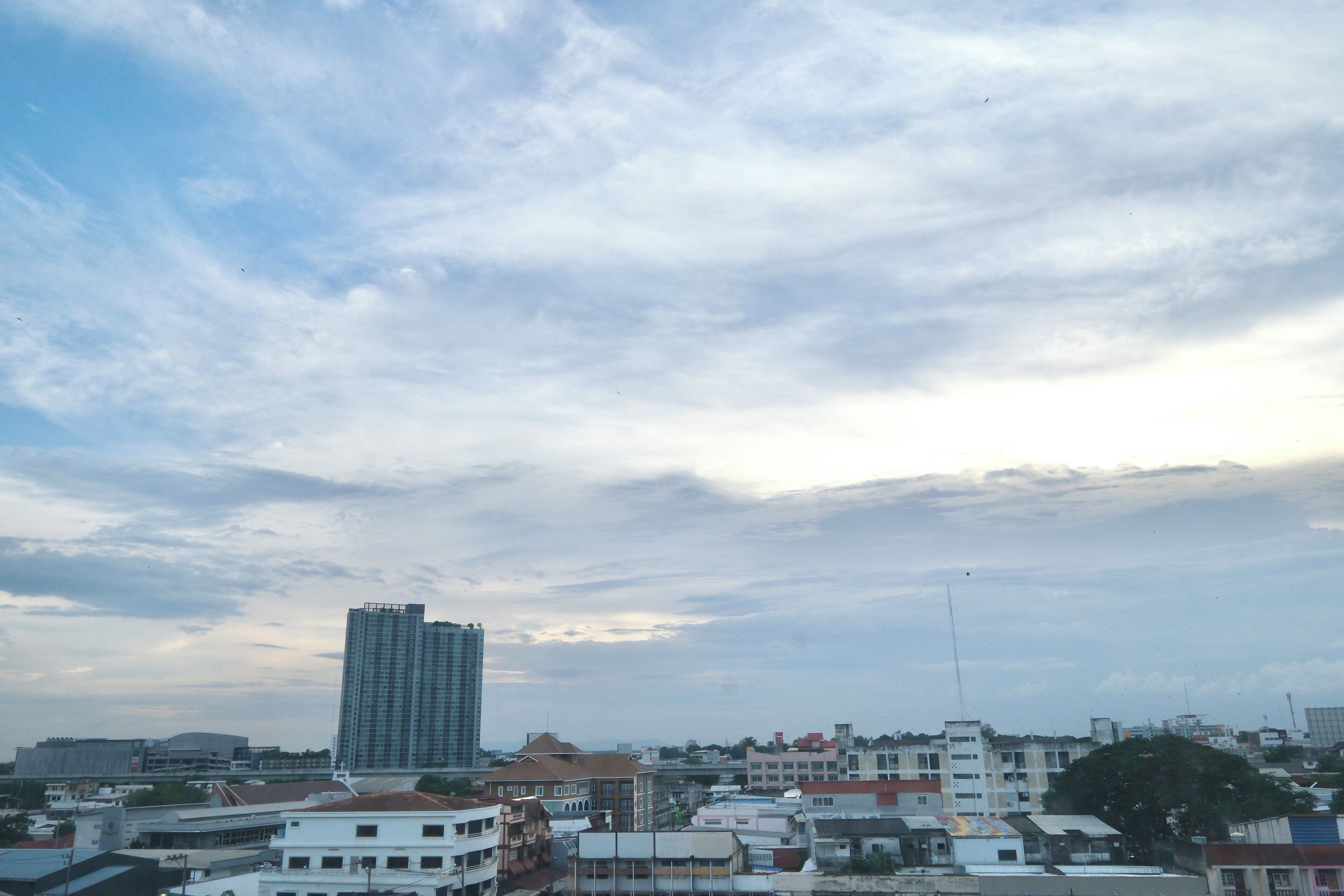 A cityscape with a prominent high-rise building, various smaller buildings, and a cloudy sky.