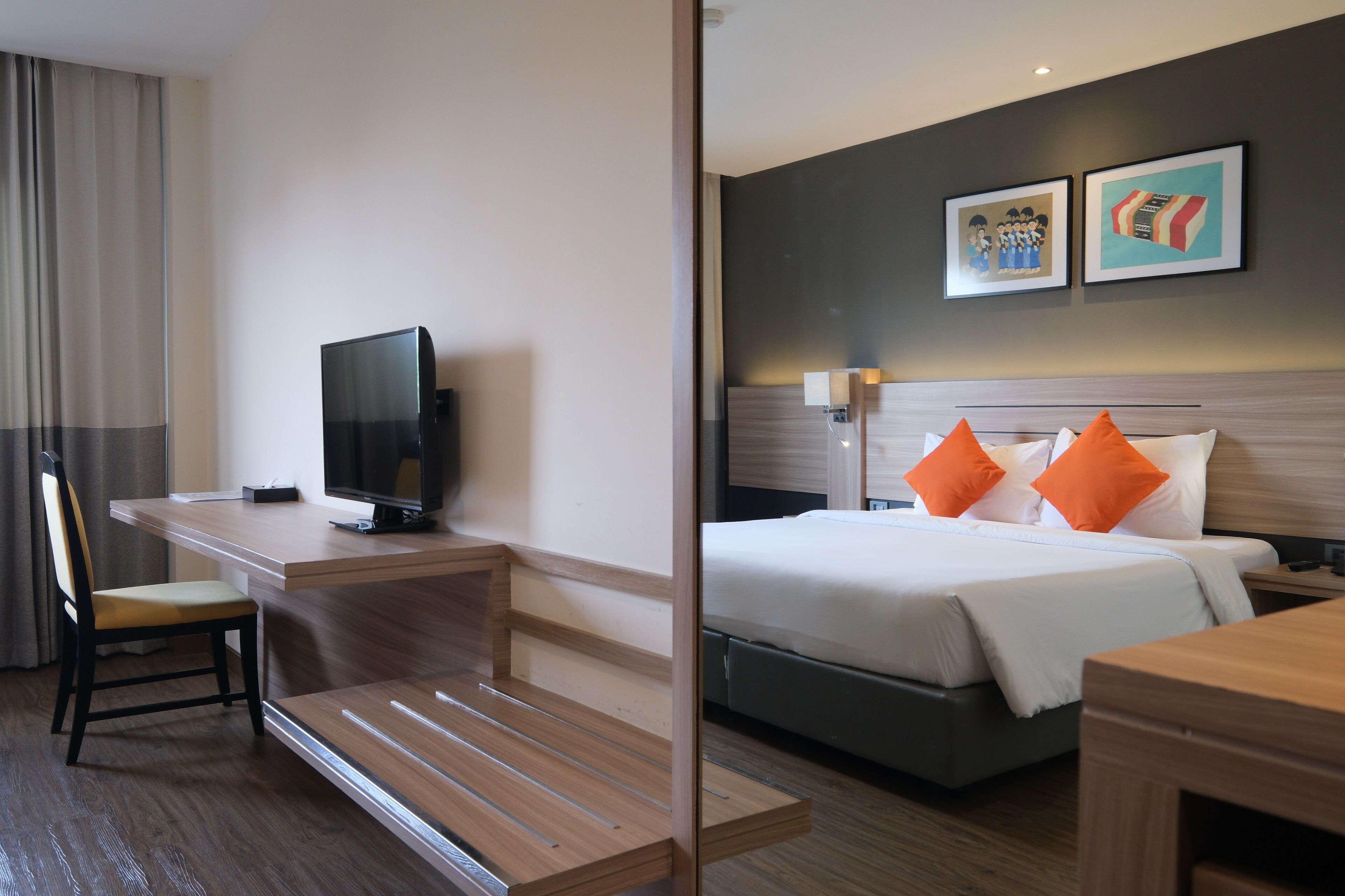 Ein Hotelzimmer mit einem Bett, einem Schreibtisch, einem Sessel, einem Fernseher und zwei gerahmten Bildern an der Wand.
