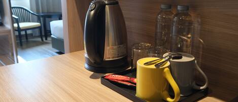 A hotel room with a wooden table, a coffee maker, a yellow mug, a white mug, and two water bottles.