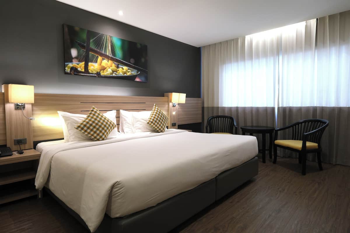 Ein Hotelzimmer mit einem großen Bett, zwei Nachttischen mit Lampen, einem kleinen runden Tisch mit einem Stuhl und einem großen Fenster mit Vorhängen.