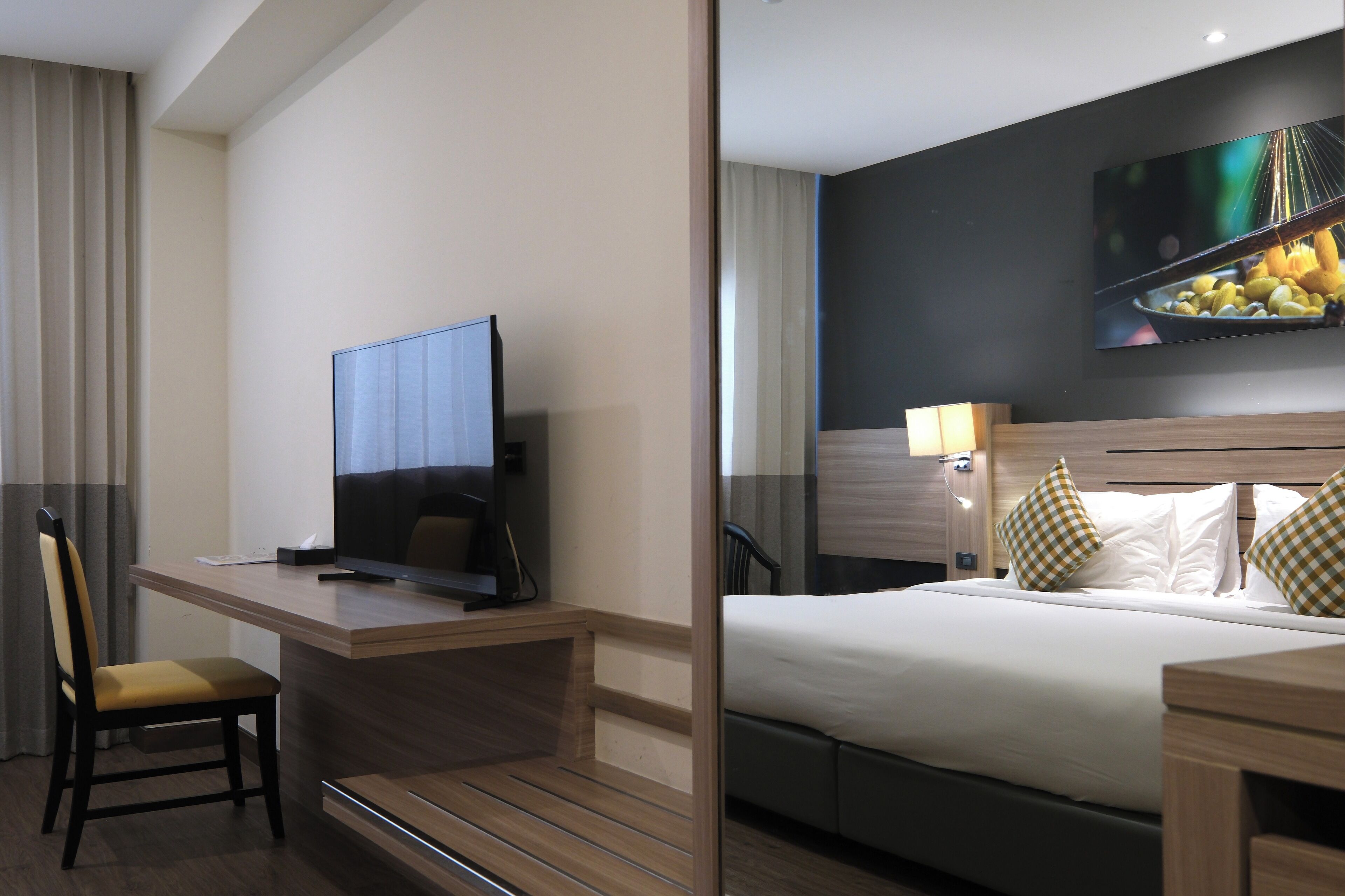 A hotel room with a bed, a desk with a television, a chair, and a wall-mounted artwork.