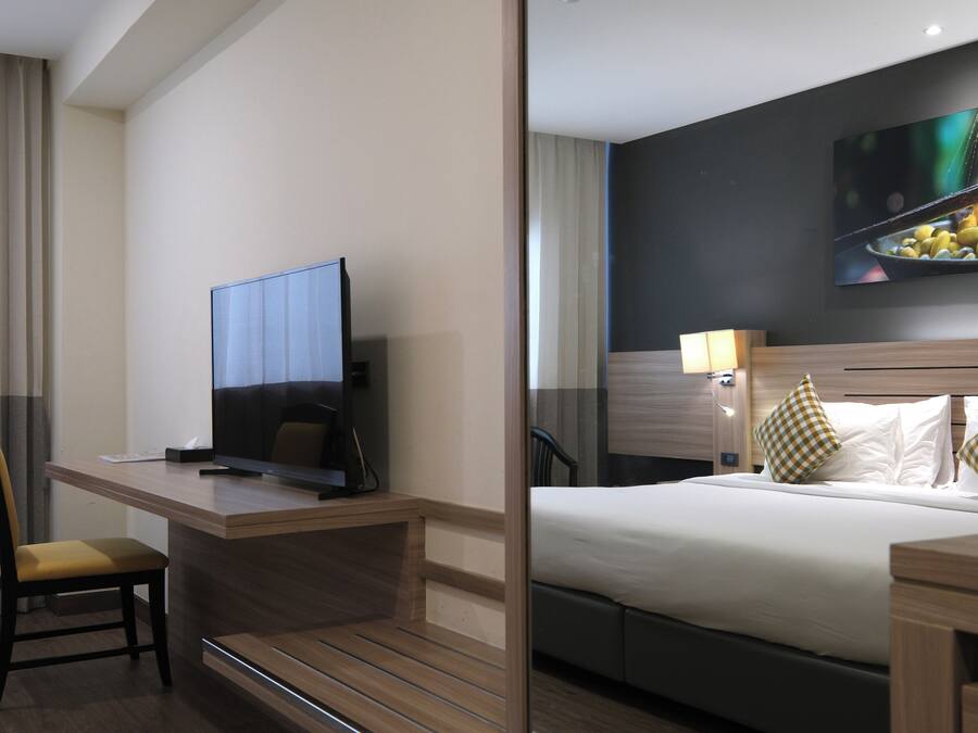 A hotel room with a bed, a desk with a television, a chair, and a wall-mounted artwork.