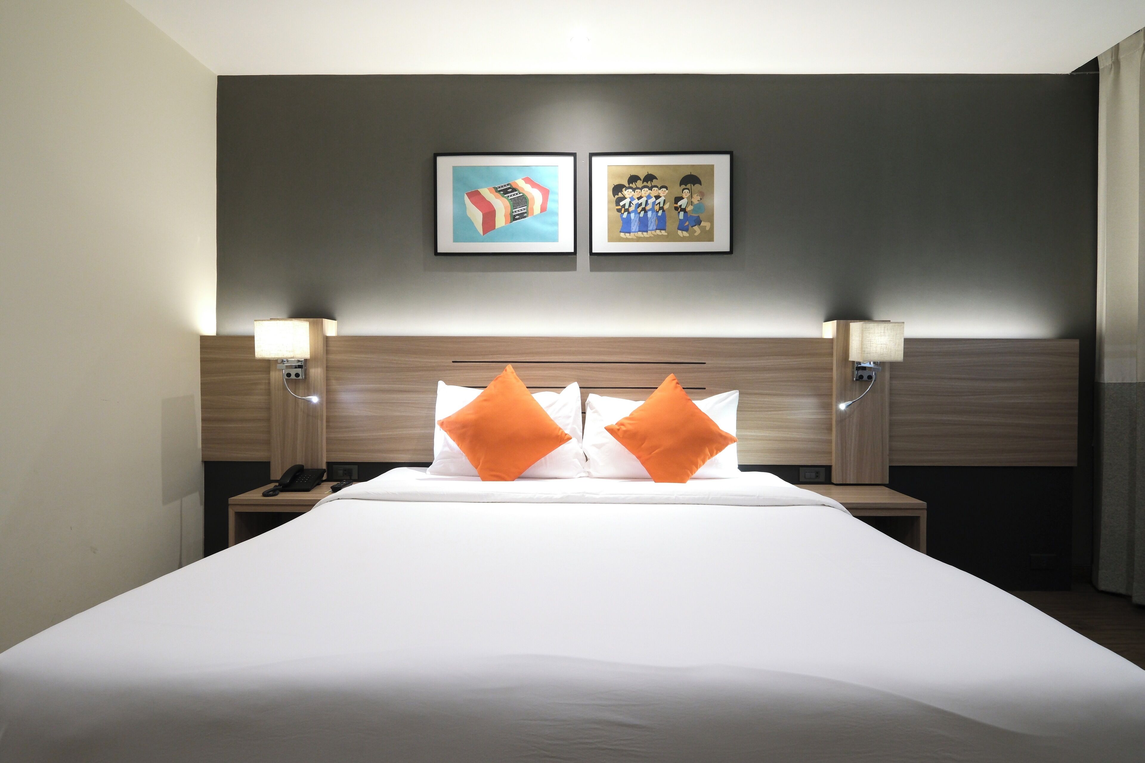 A hotel room with a large bed, two pillows, a nightstand with a lamp, and two framed pictures on the wall.