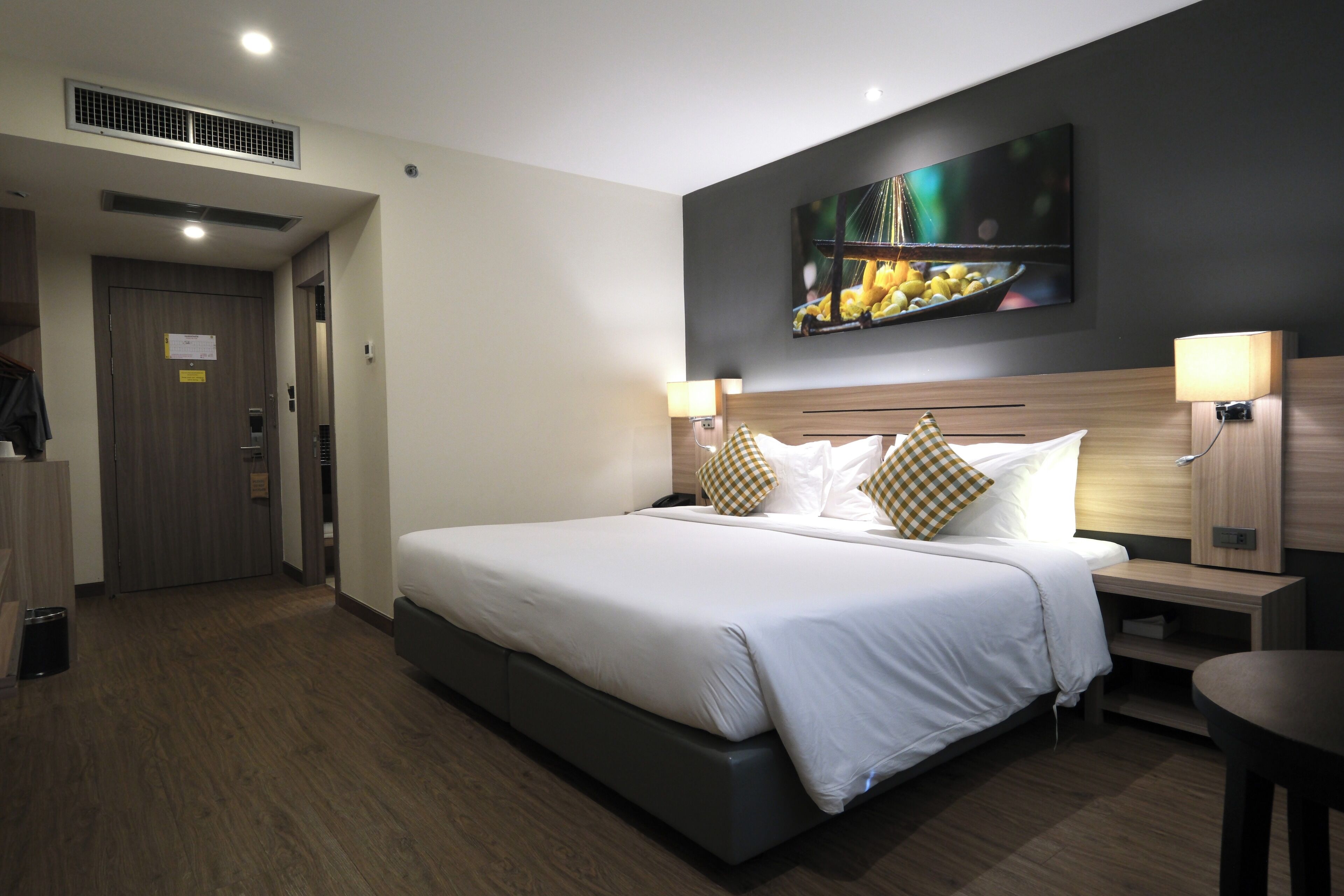 A hotel room with a large bed, two bedside tables, a wall-mounted TV, and a door to the left.