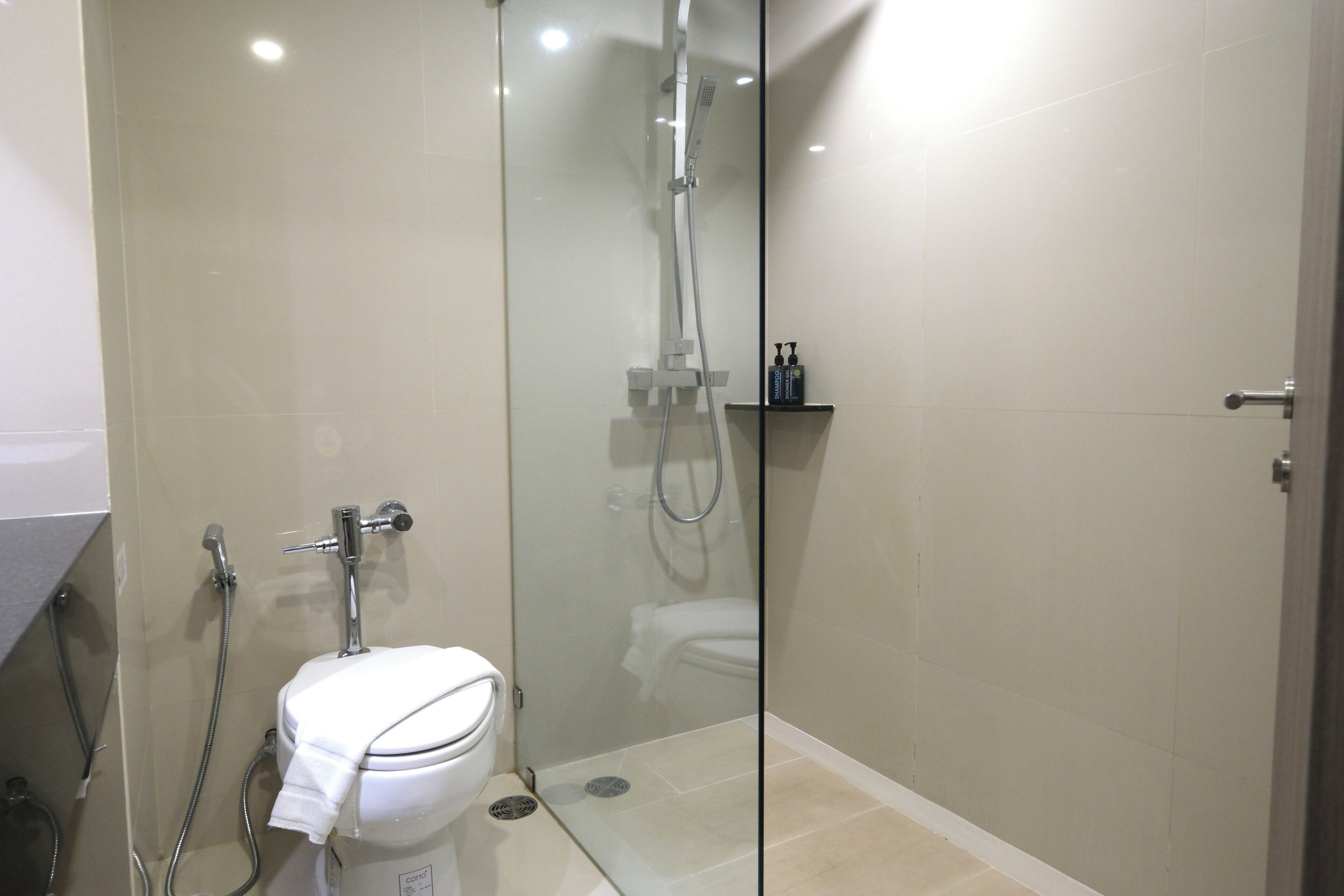 A modern bathroom with a glass-enclosed shower, a toilet, and a small shelf with toiletries.