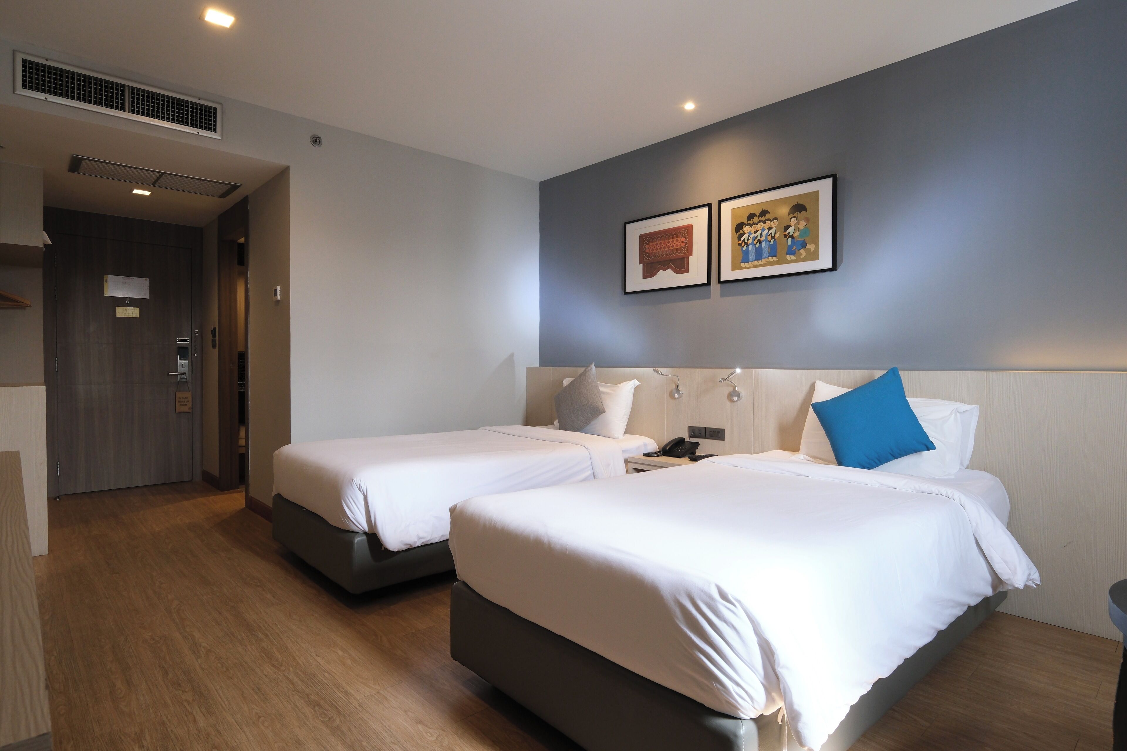 A hotel room with two beds, a desk, a chair, and a wall-mounted artwork.