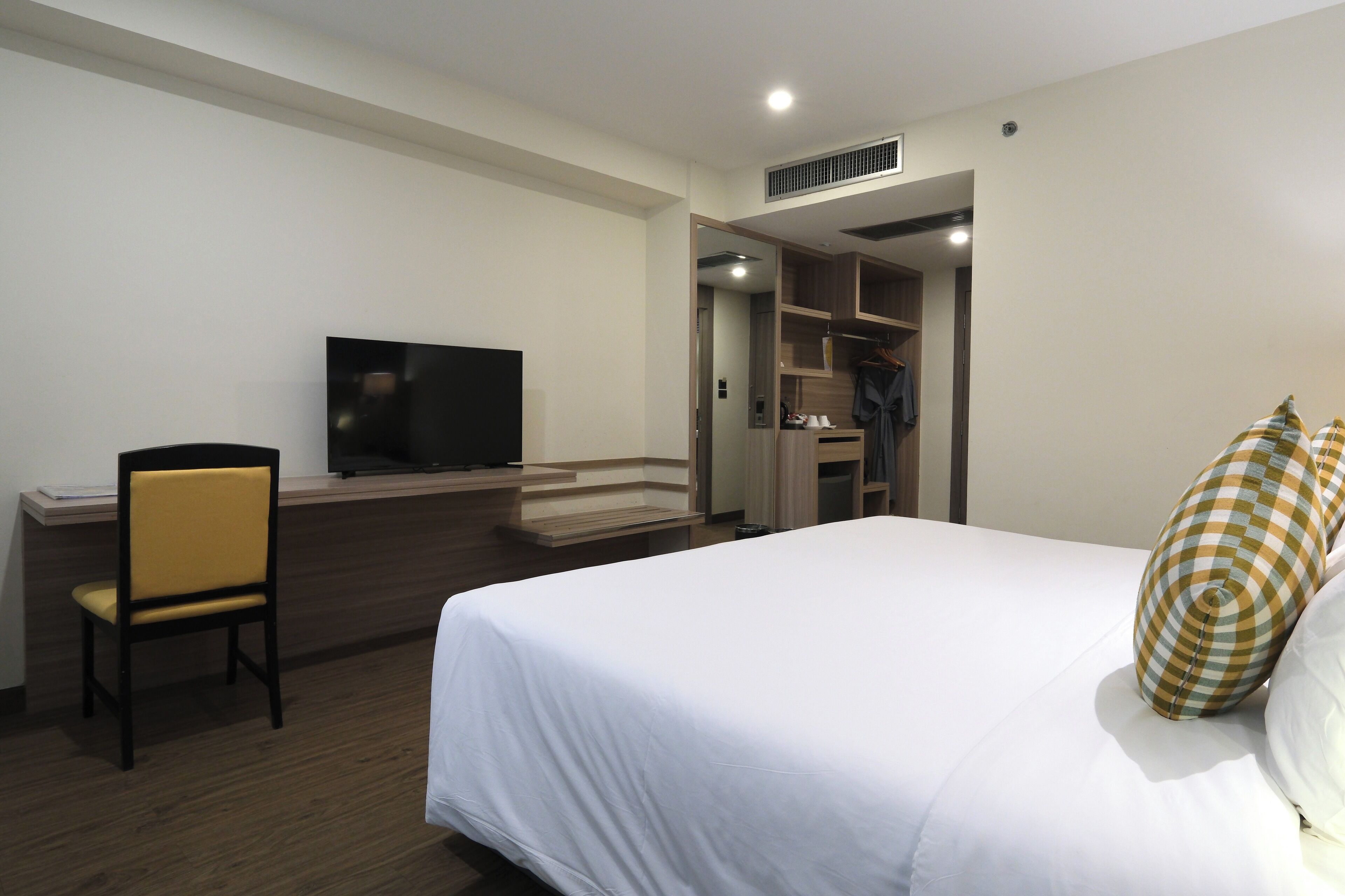 A hotel room with a bed, a TV, a desk with a chair, and a walk-in closet.