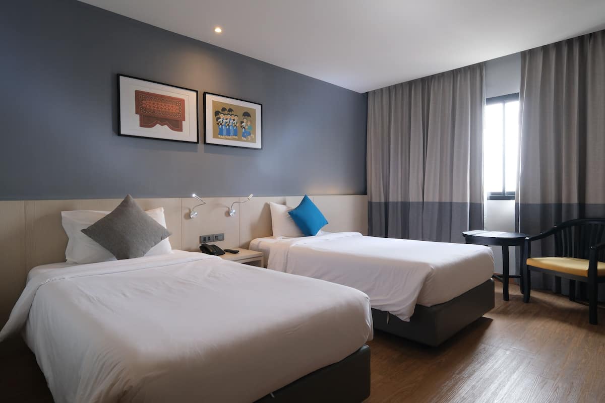 Ein Hotelzimmer mit zwei Betten, einem kleinen Tisch, einem Stuhl und einem Fenster mit Vorhängen.