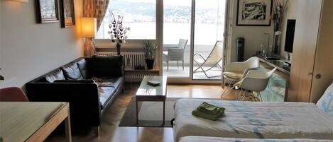 A hotel room with a bed, a sofa, a desk, a chair, a balcony with a view, and a television.