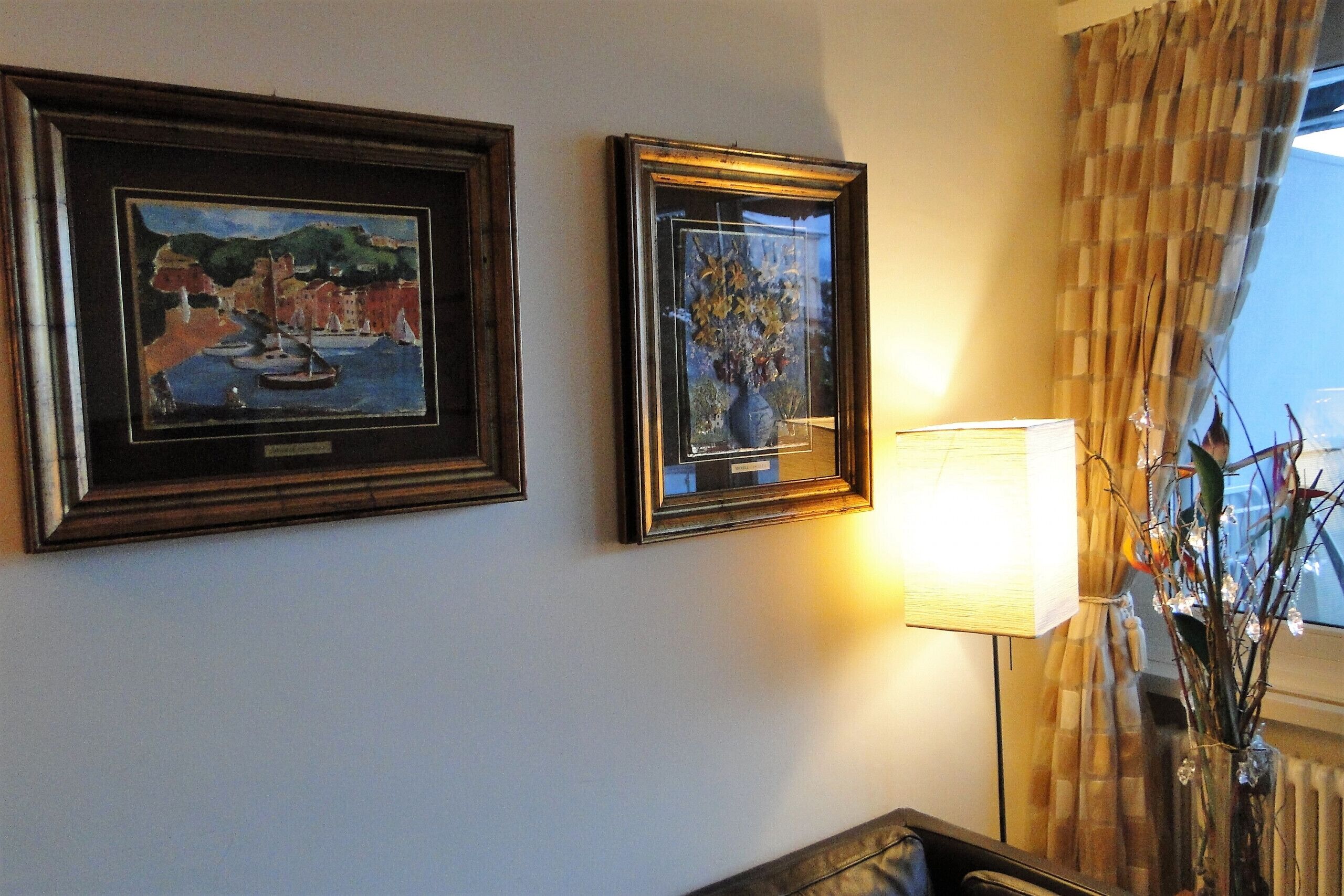 Two framed artworks on a wall, a lamp, and a window with curtains.