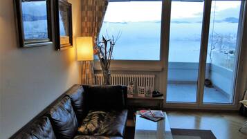 Un salon avec un canapé en cuir, une table basse, une lampe et une vue sur la mer grâce à de grandes fenêtres.