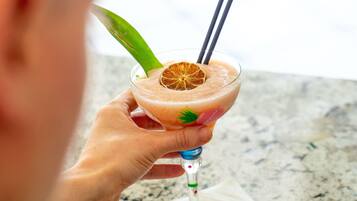 A person holding a cocktail with a straw and a slice of orange garnish.