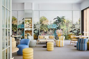 A modern living room with a tropical mural, comfortable seating, and a visible bookshelf.