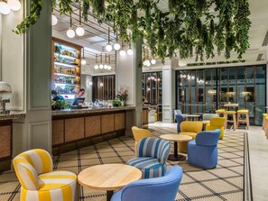 A bar area with a bartender, seating with yellow and blue chairs, hanging plants, and a patterned floor. - The Adnate Perth - Art Series (Perth)