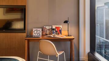 Een moderne hotelkamer met een houten bureau, een witte stoel, een zwarte vloerlamp en kunst aan de muur.