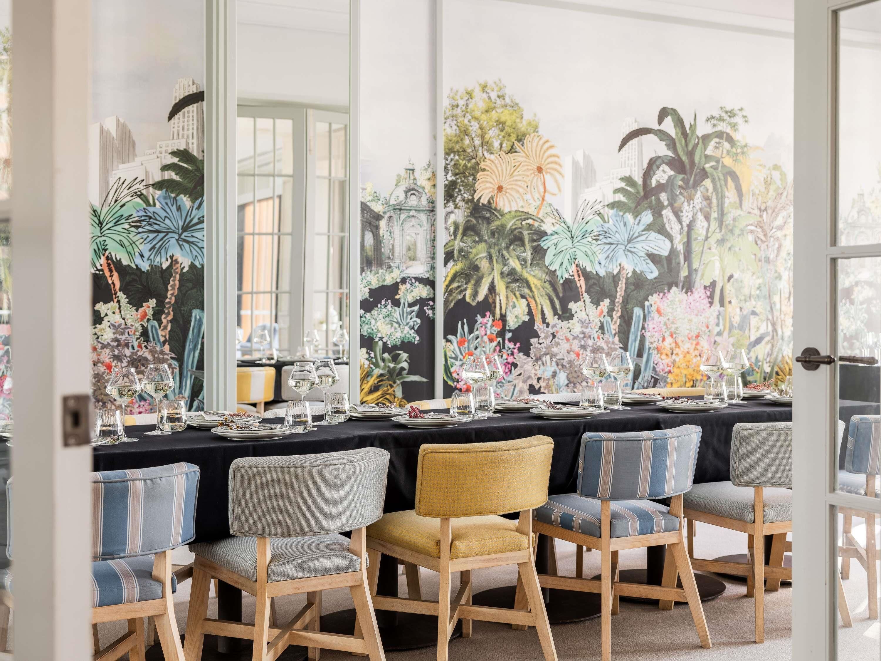 A dining area with a table set for six, chairs with cushioned seats, and a large window with a view of buildings and palm trees.