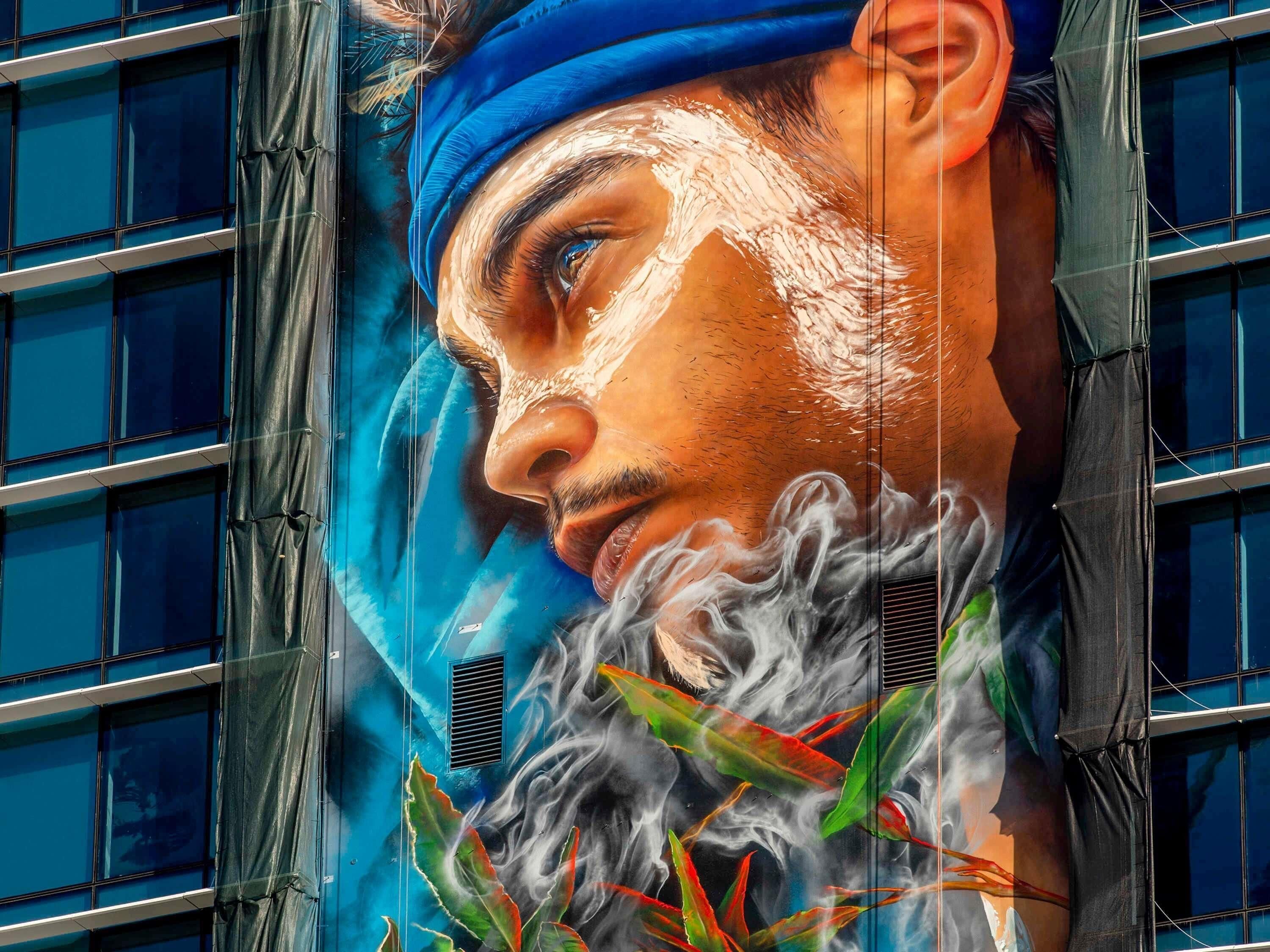 A building facade with a large mural of a person wearing a blue headscarf and a beard.