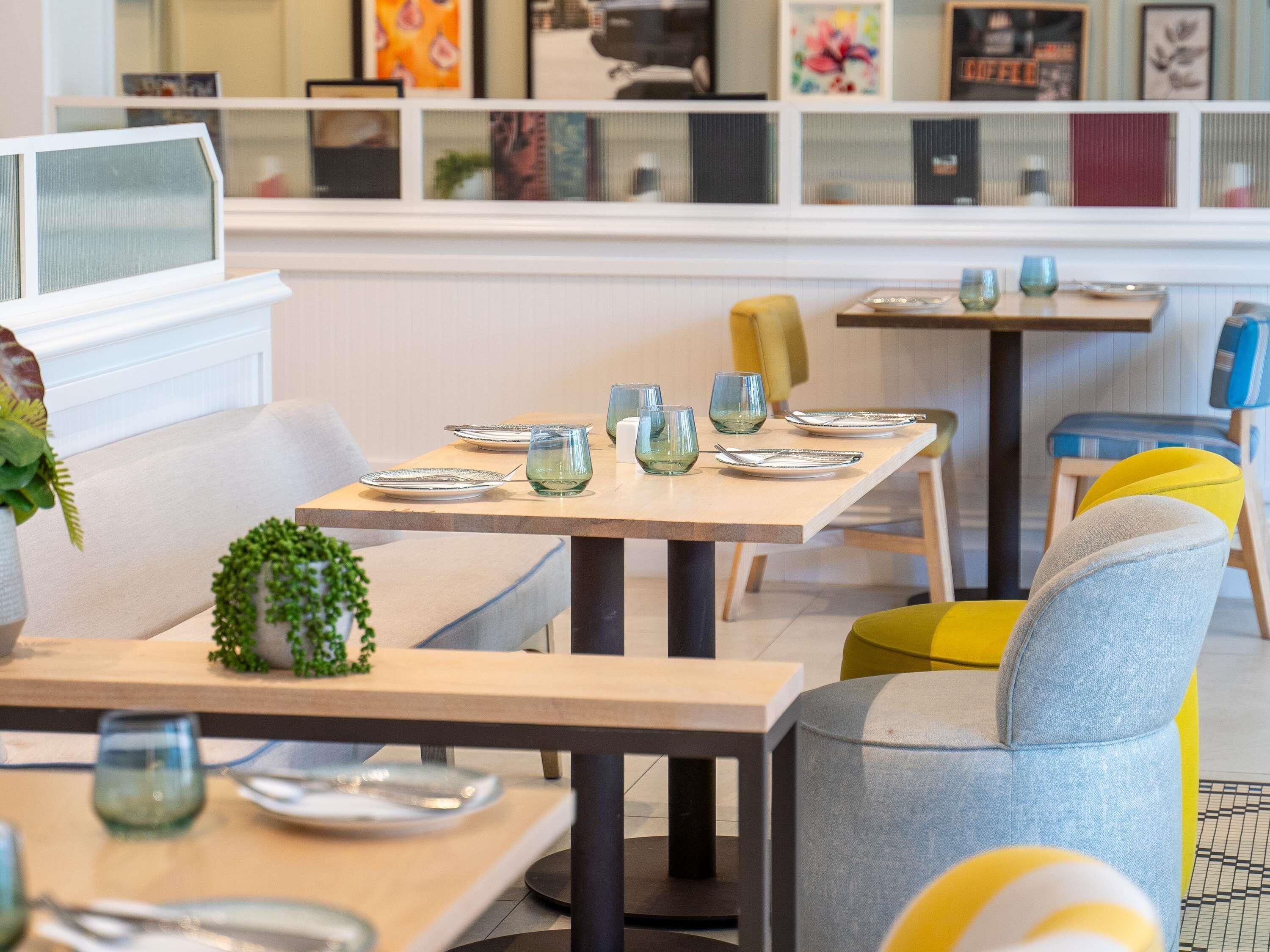 Un área de comedor moderna con mesas preparadas para dos personas, con vasos y platos.