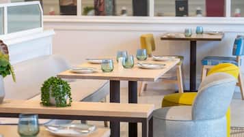 Un área de comedor moderna con mesas preparadas para dos personas, con vasos y platos.