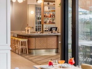 Zona de bar con taburetes, una barra llena de botellas y vistas a través de un ventanal.
