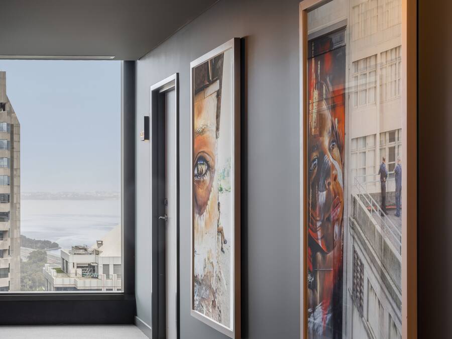 Un corridoio con opere d'arte incorniciate alle pareti, una porta e vista su edifici e uno specchio d'acqua attraverso un'ampia finestra.