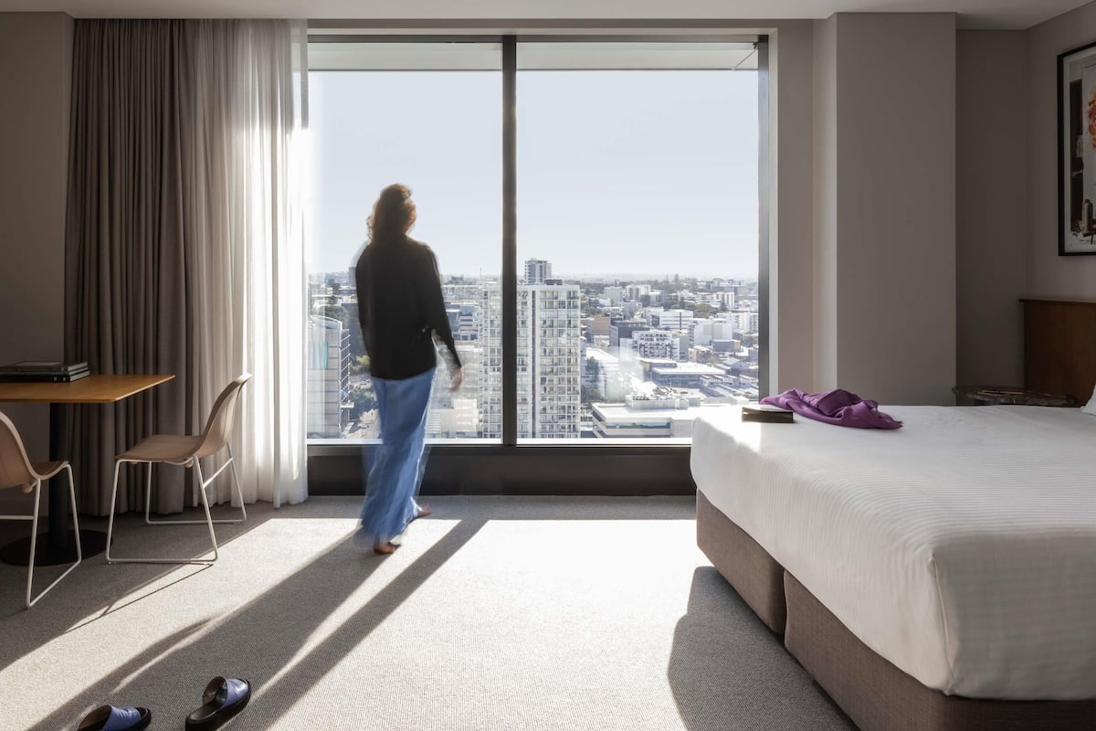 Habitación de hotel con un ventanal grande, cama, escritorio y silla.