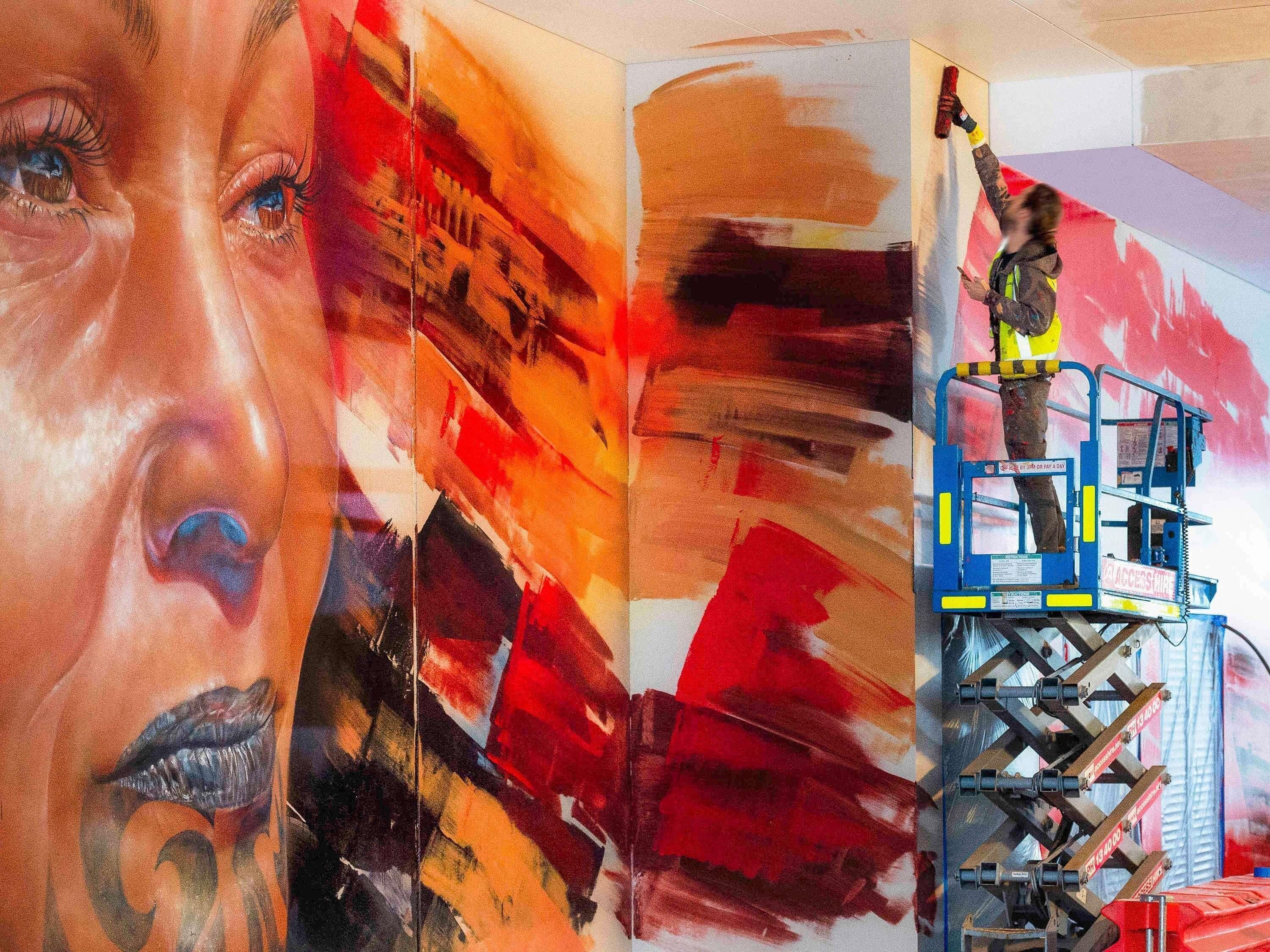 Un mural con arte abstracto y una persona pintando en un andamio.