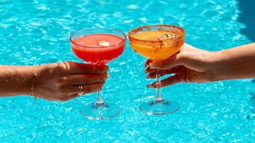 Dos manos sosteniendo copas de cóctel sobre una piscina.