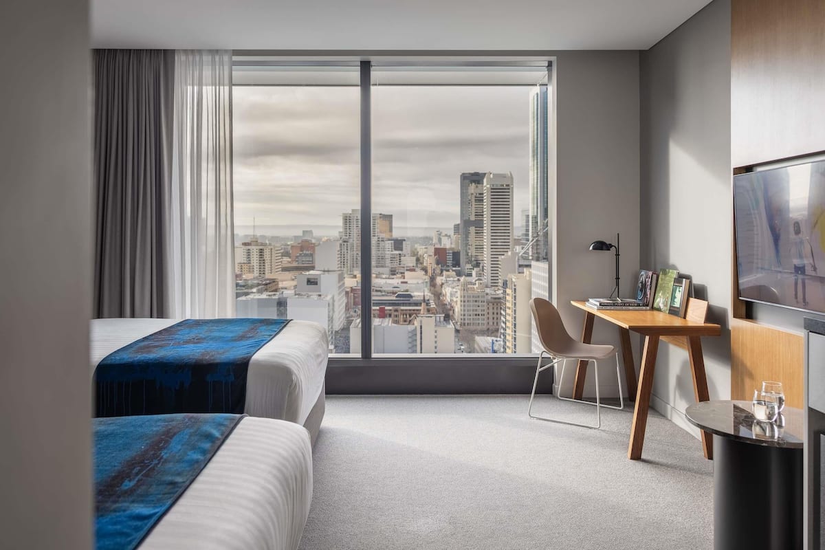 Una habitación de hotel con un ventanal grande, una cama, un escritorio, una silla y un televisor.