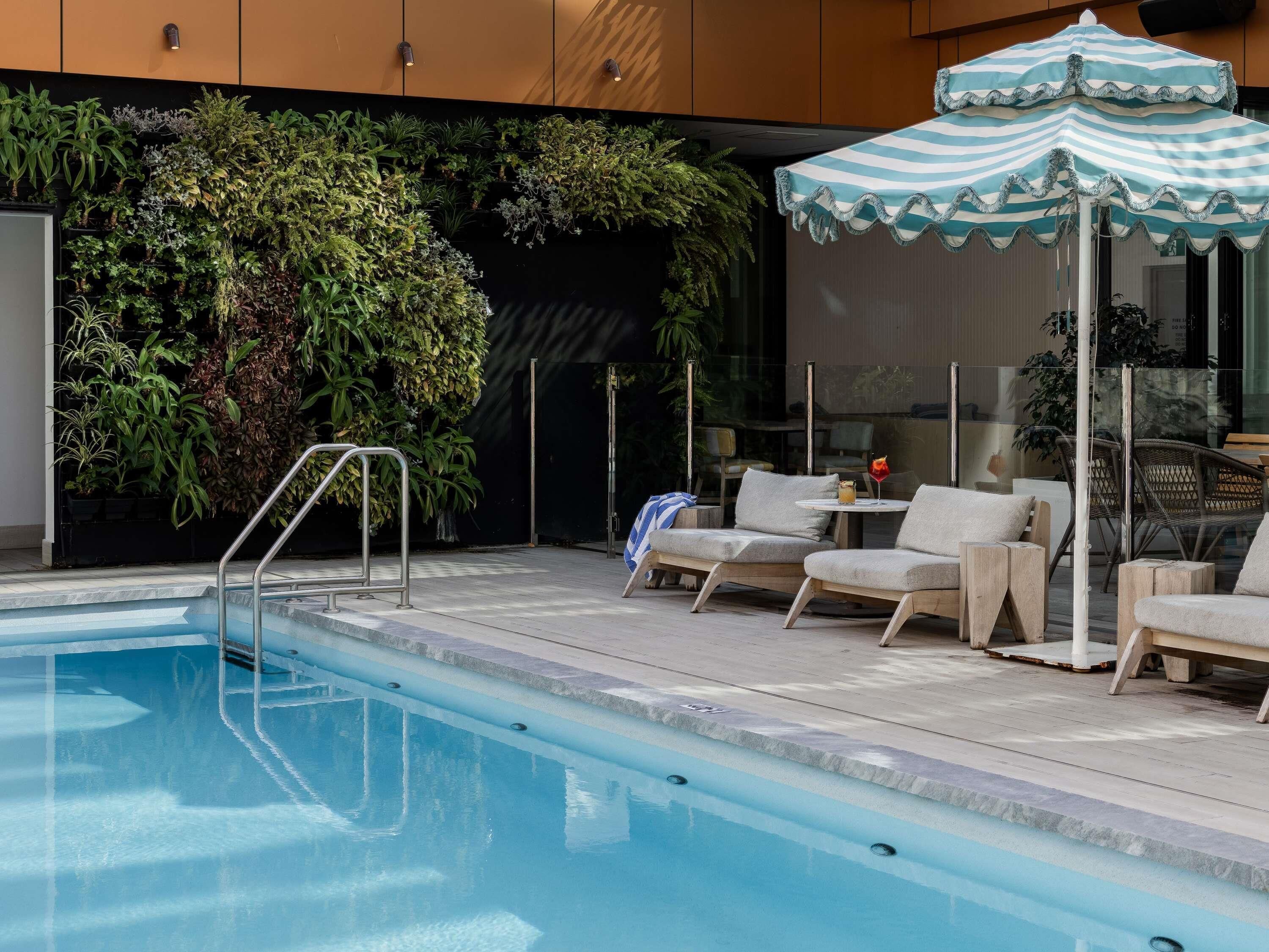 Un área junto a la piscina con sillones de descanso, una mesita y un paraguas decorativo.