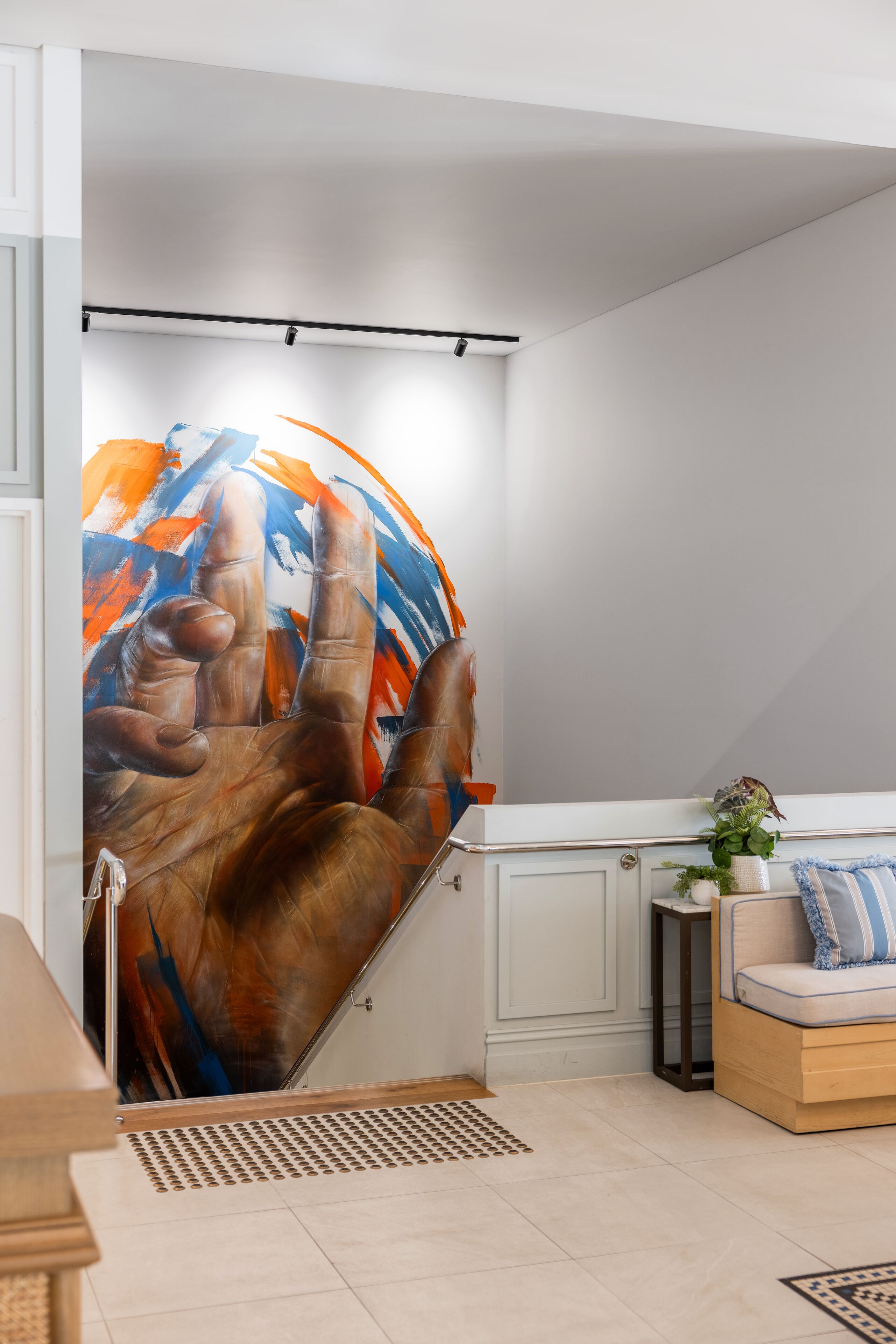 Una habitació amb un quadre abstracte gran a la paret, una panxa de fusta, una taula petita amb una planta i un armari blanc.