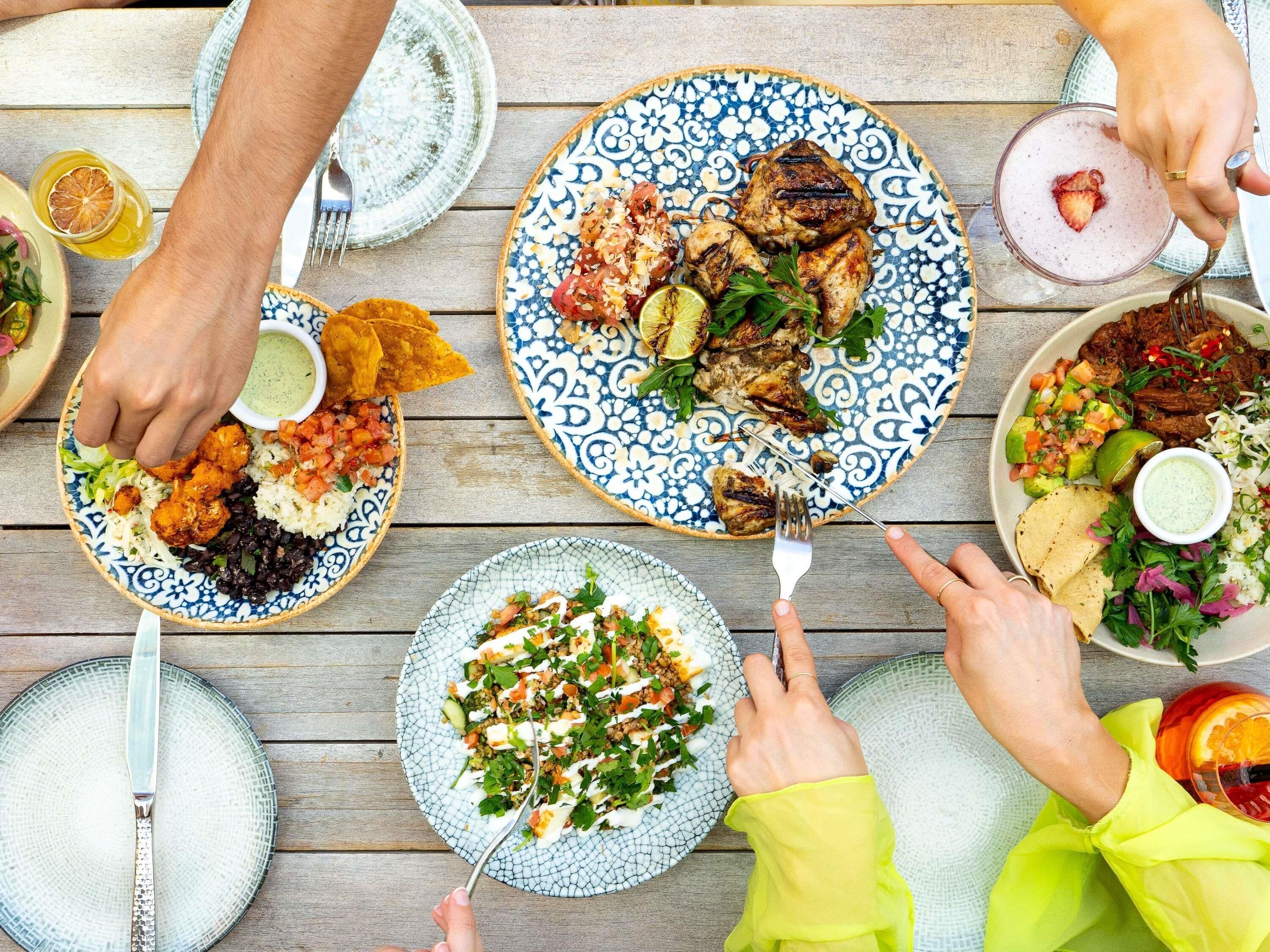 Una mesa de comedor con varios platos de comida, cubiertos y una persona que lleva una manga amarilla brillante.