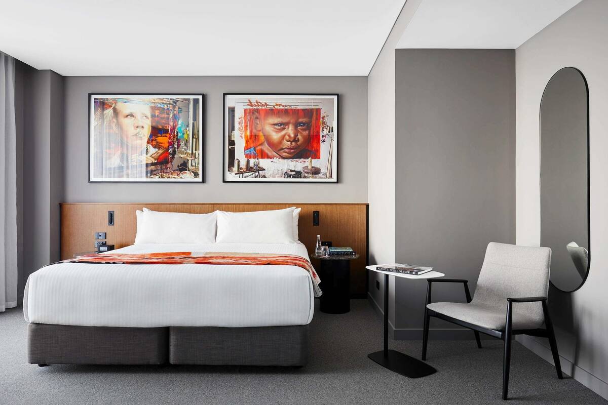 Una habitación de hotel moderna con una cama grande, una mesita de noche, una silla y dos cuadros enmarcados en la pared.