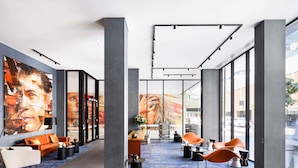 A modern lobby with large windows, a seating area with orange chairs, and a blue carpet. - The Adnate Perth - Art Series (Perth)